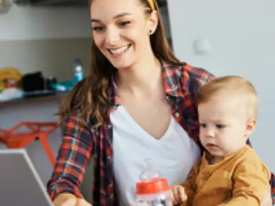 mom holding her baby while smiling at a computer