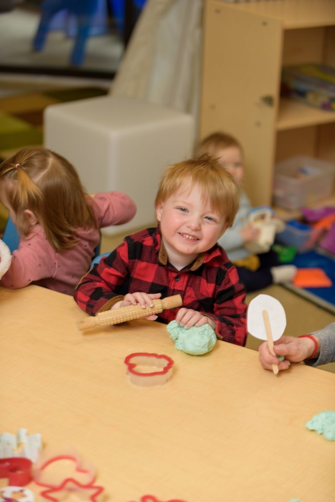 children sitting around a table playing, one boy smiling at the camera