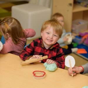 children sitting around a table playing, one boy smiling at the camera